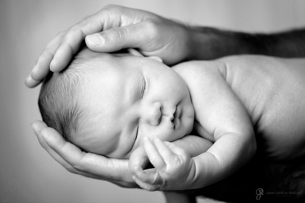 Bebé durmiendo entre las manos de su padre